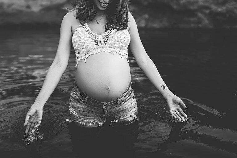 Black and white photo of a pregnant woman with her belly exposed in a river