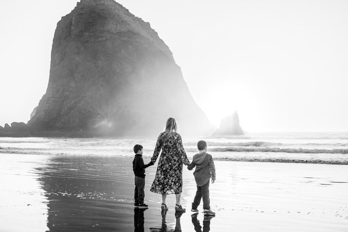 Black and white image of mom and sons standing in front of Haystack Rock .