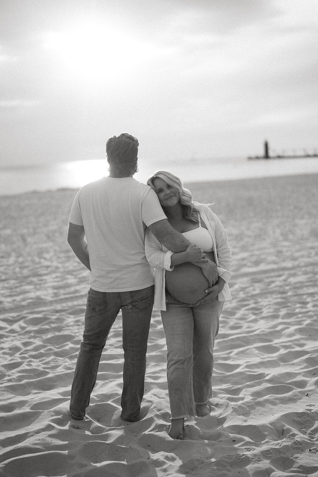 Silhouette of pregnant couple hugging on South Haven North Beach at sunset, Lake Michigan in background.