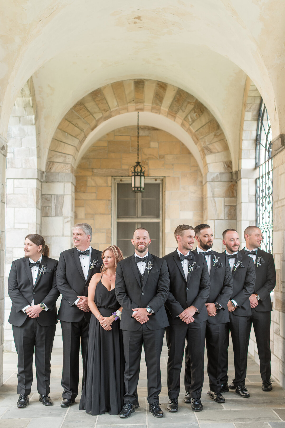 Groom with his groomsmen and best woman all wearing black and standing in a v-shape outside Catholic church.