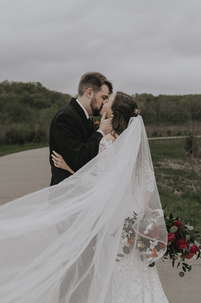 bride and groom kissing as veil flows in the wind