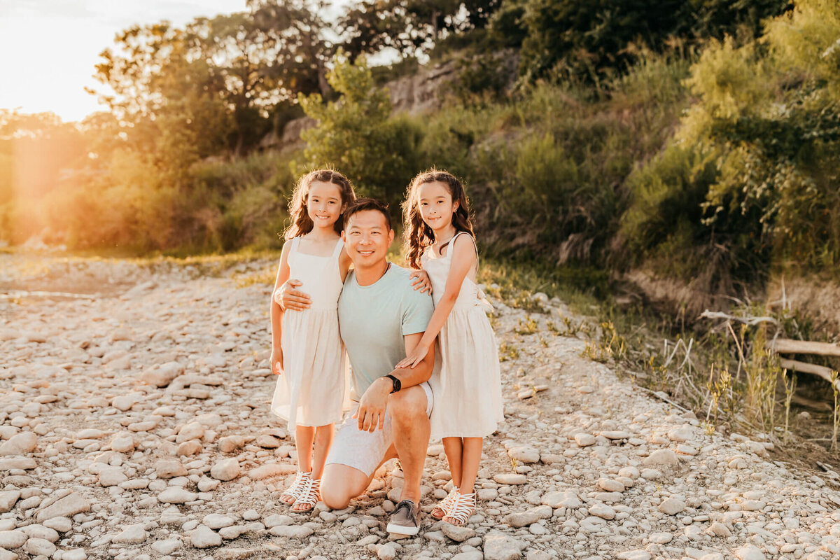 dad kneels down on white rocks while holding his twin daughters.