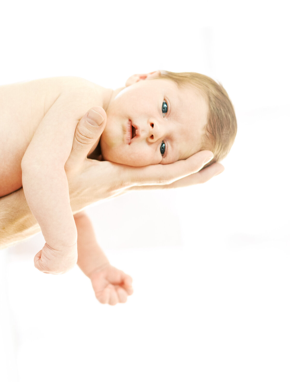 Portrait of a shirtless newborn baby lying on palm of a mans hands.
