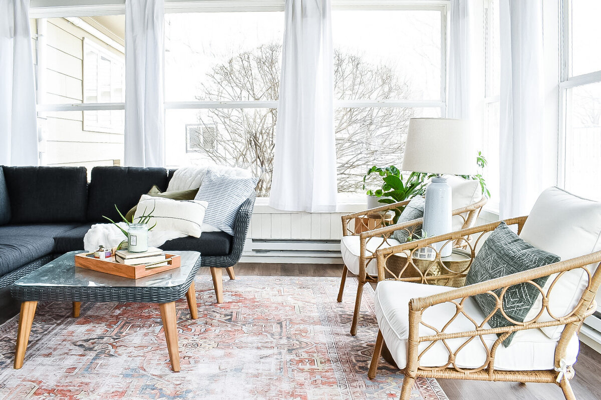 Two white wicker patio chairs sit in a bright sunroom