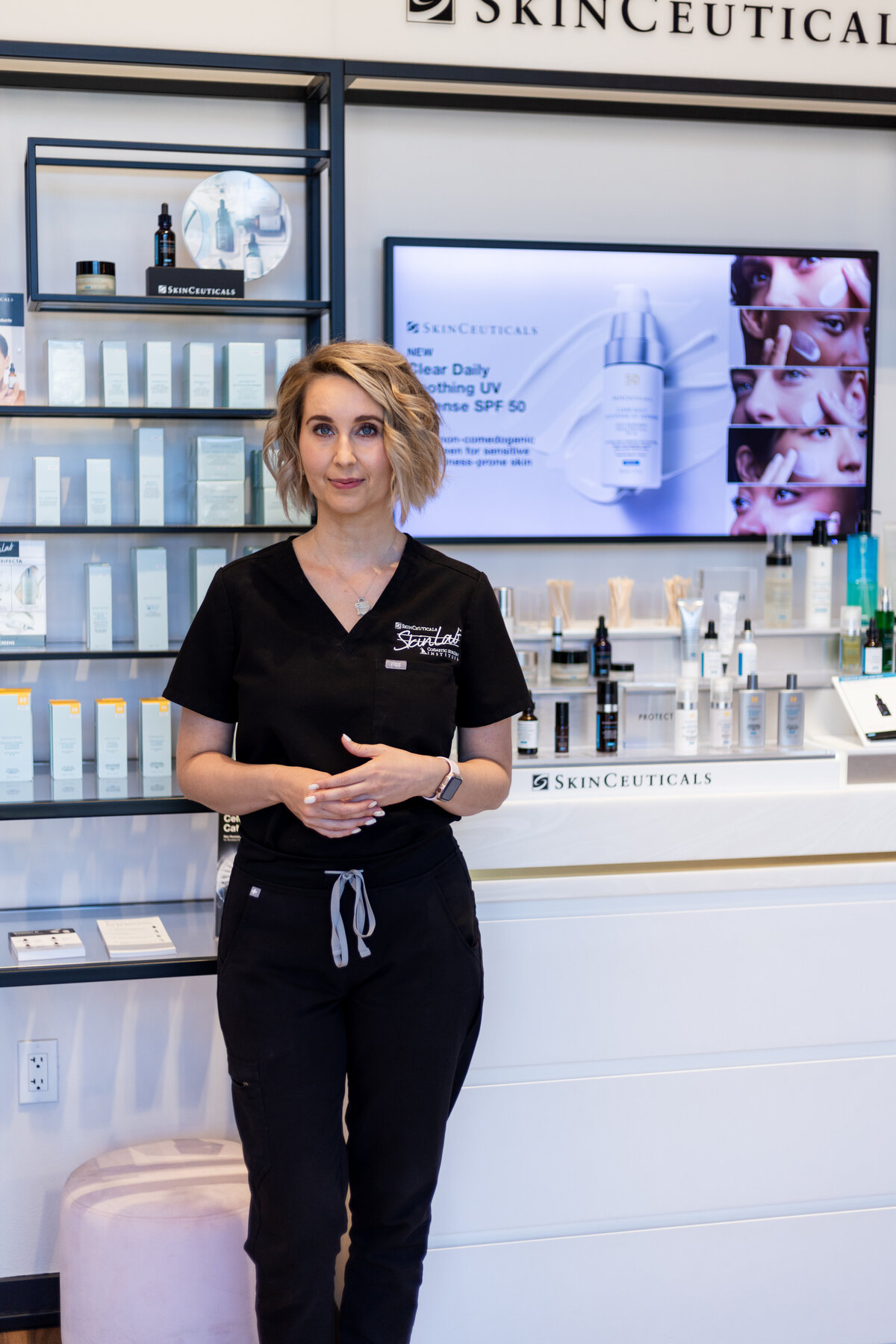 Ethetician in black scrubs in salon standing next to product counter