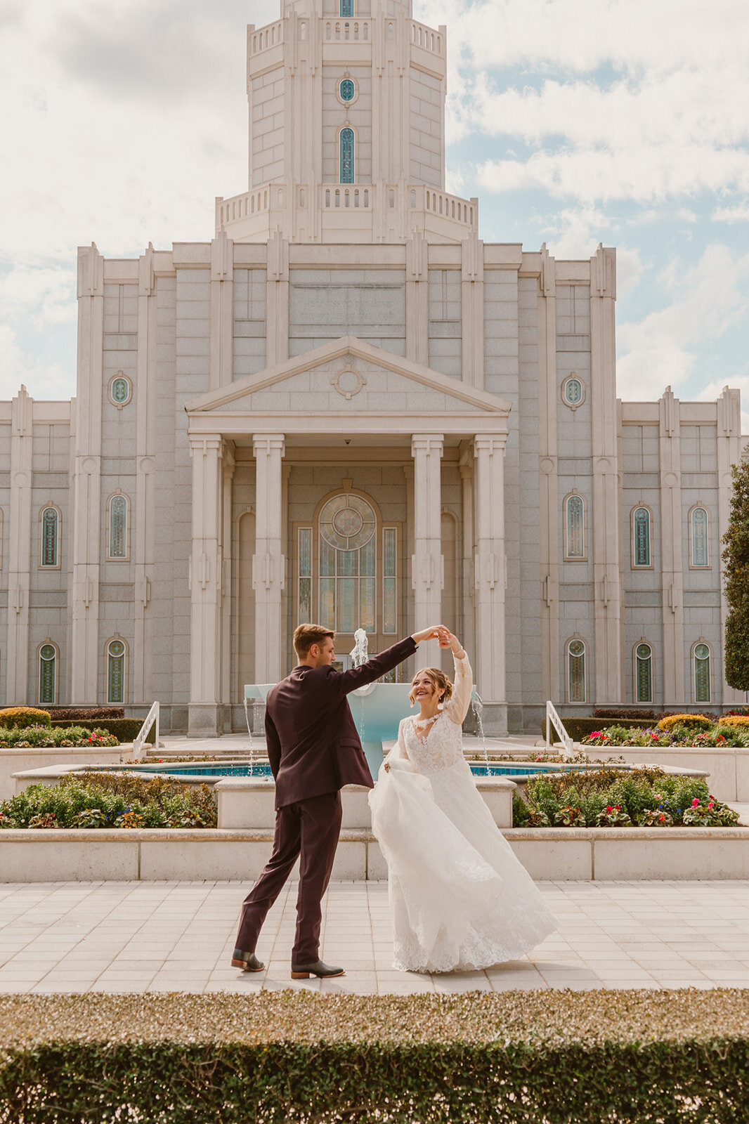 A newlywed couple dances in front of the grand entrance of the LDS Houston Temple, showcasing elegant architecture and classic wedding attire. 