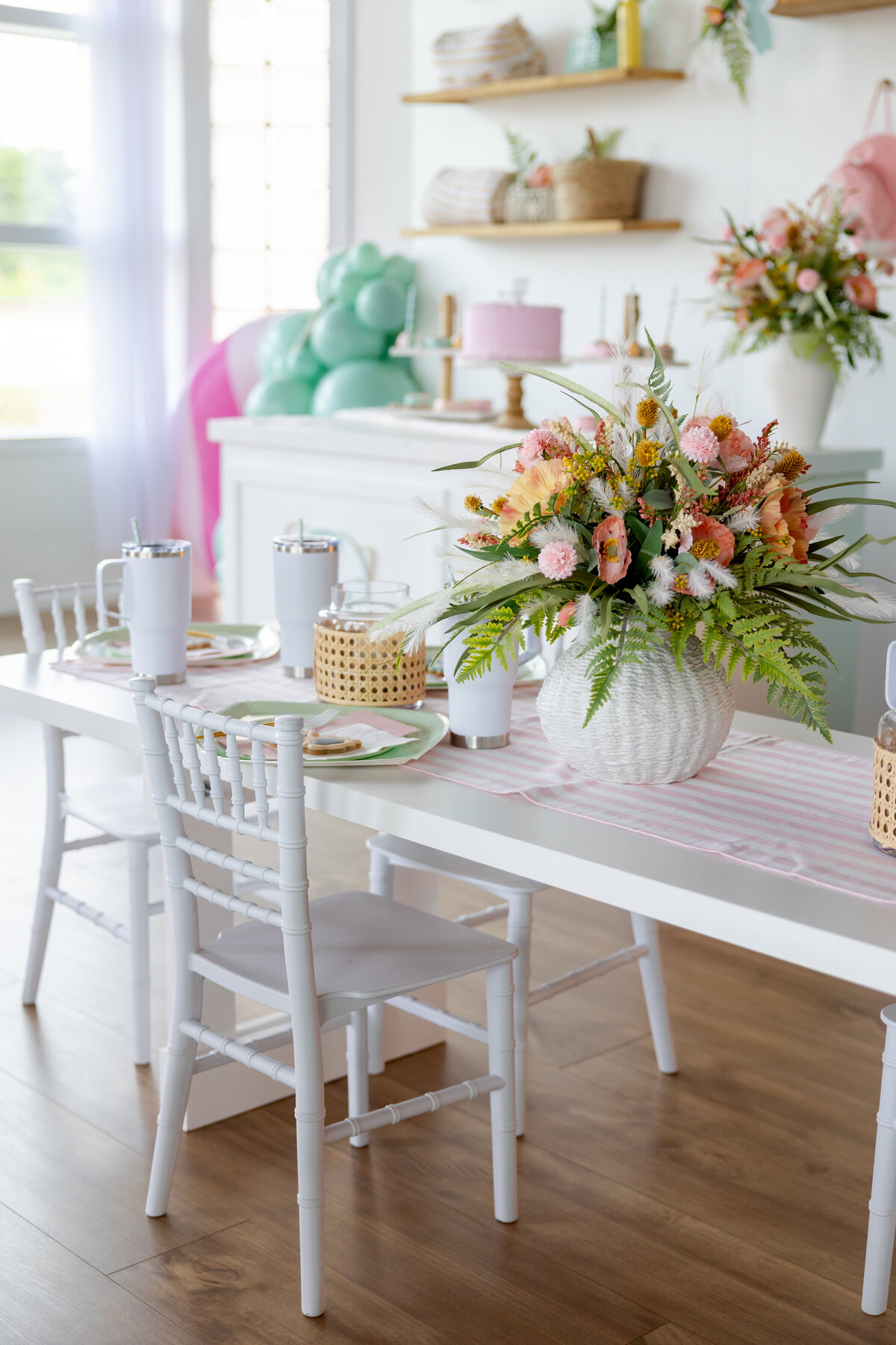 Decorated kids table with pool flowers, white table and chairs, and kid white tumblers. 