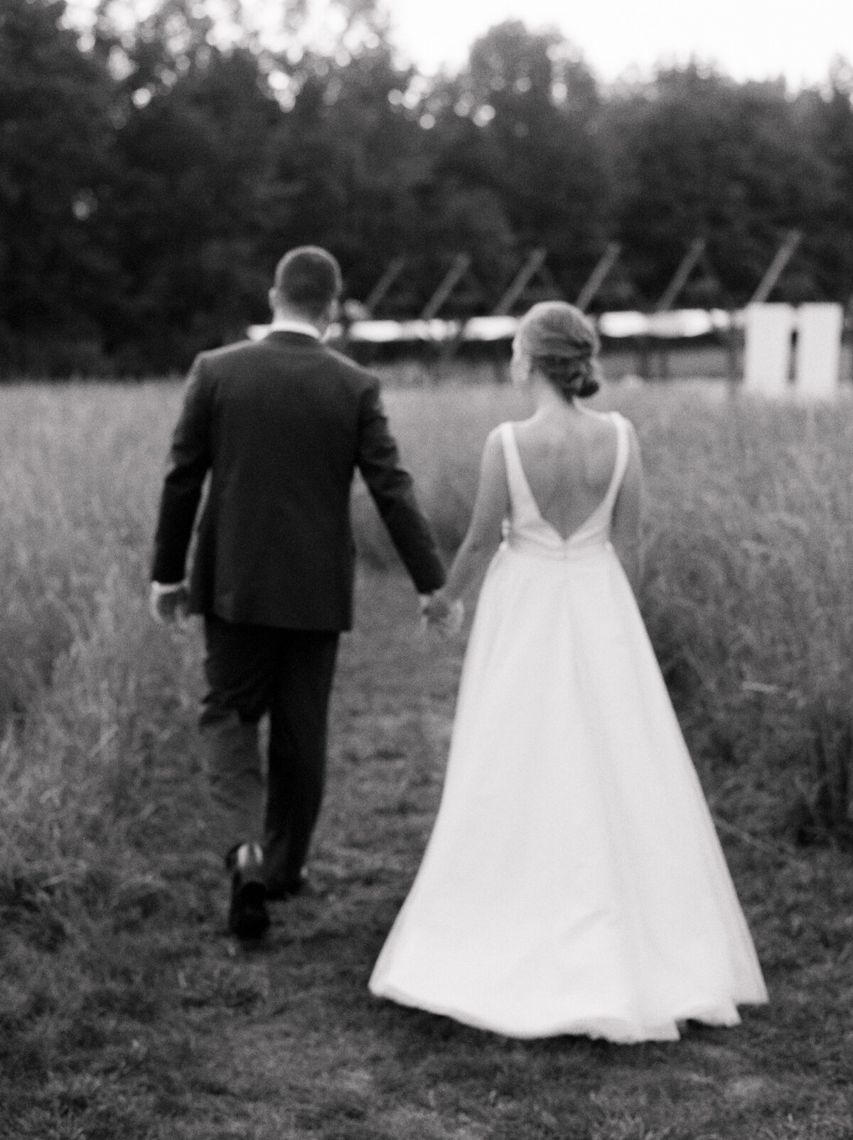 Black and white photo of a bride and groom holding hands and walking away from the camera