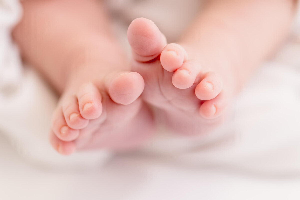 Close-up of a babys feet resting on a soft white blanket. The focus is on the tiny toes and delicate skin, conveying a sense of warmth and innocence.