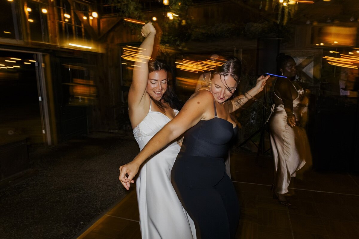Bride and bridesmaid dancing and laughing on the dance floor at night