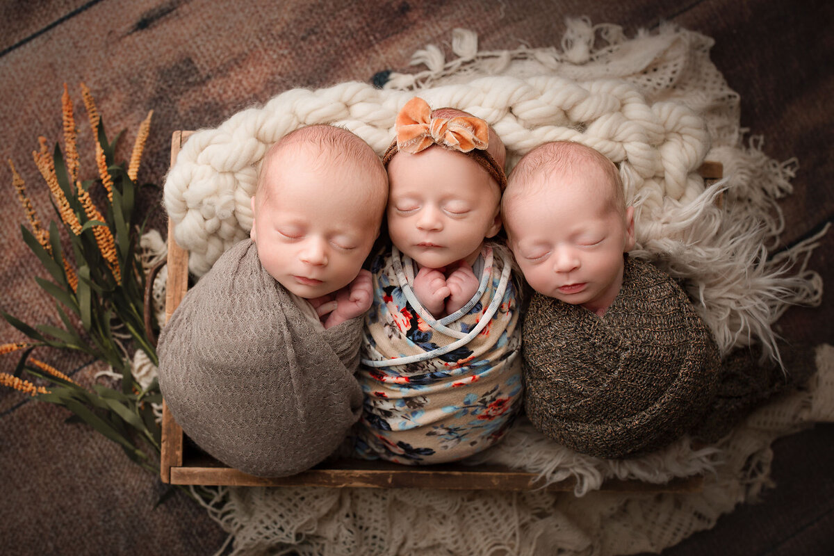 triplets snuggled together in a basket wrapped in cute swaddles
