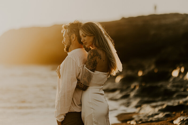 Femme enlaçant son mari de dos sur fond de coucher de soleil lors d'une séance photo couple en Vendée.