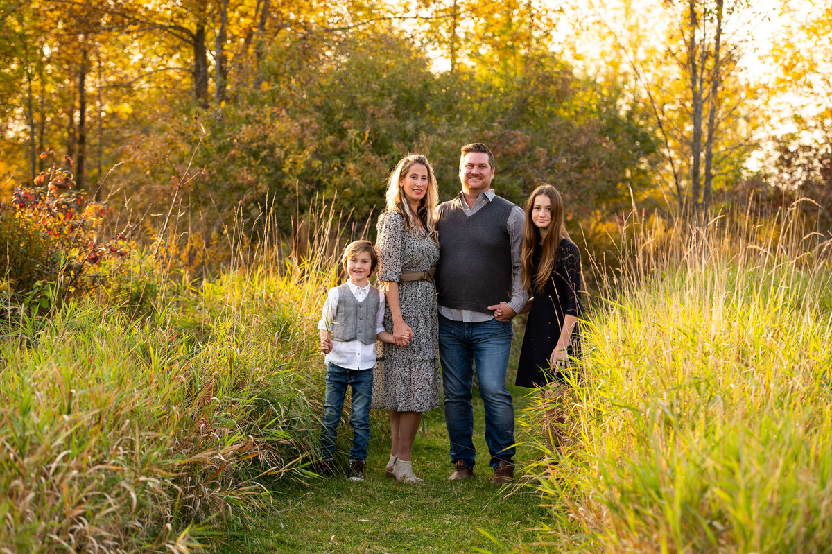 a family standing together in a grassy field at sunset golden hour captured by Ottawa family photographer JEMMAN Photography