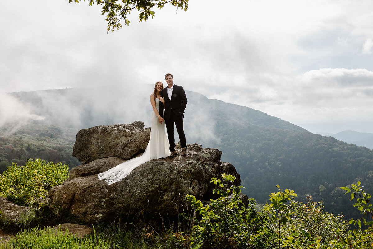 A couple standing together on a boulder on a mountain