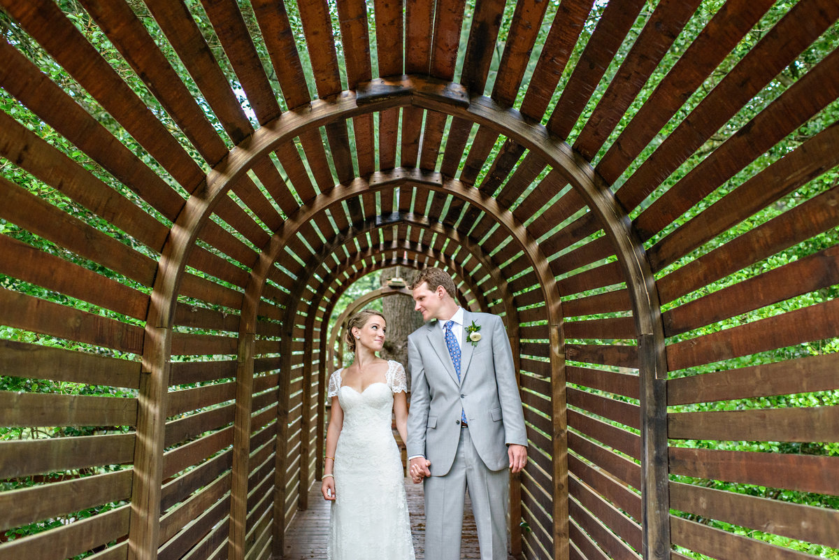 A couple under a covered bridge hold hands after their Tyler Arboretum Wedding.