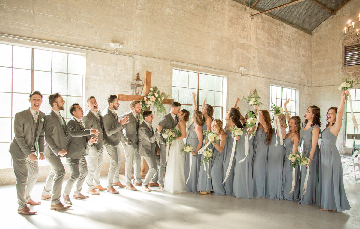 The large wedding party celebrate as the bride and groom kiss