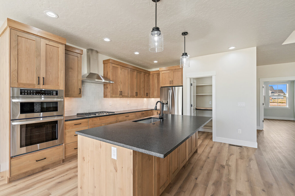 newly modeled kitchen  with light wooden cabinets and black counter tops with three stool bar