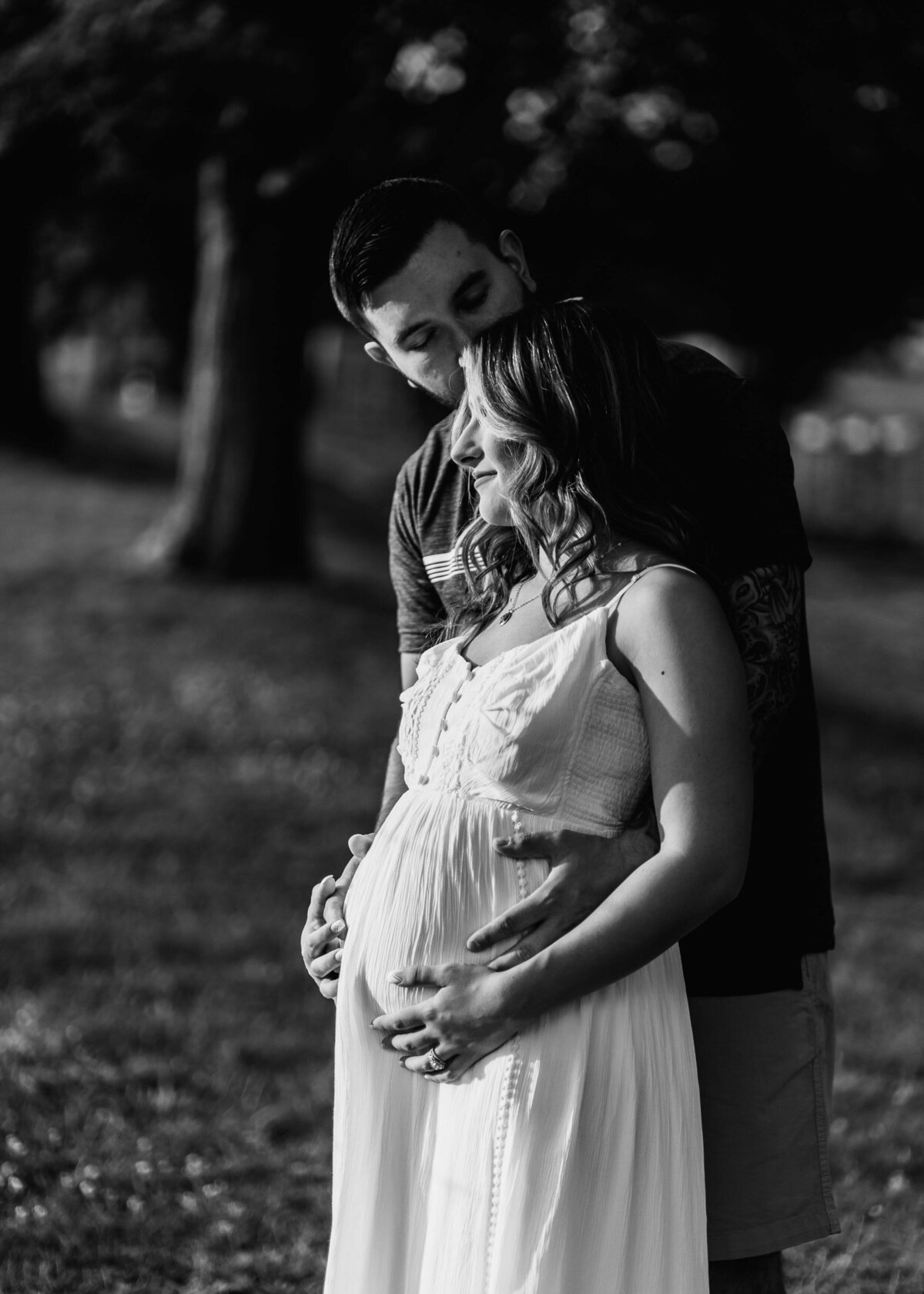 A pregnant couple embracing in a park captured by a Pittsburgh maternity photographer.