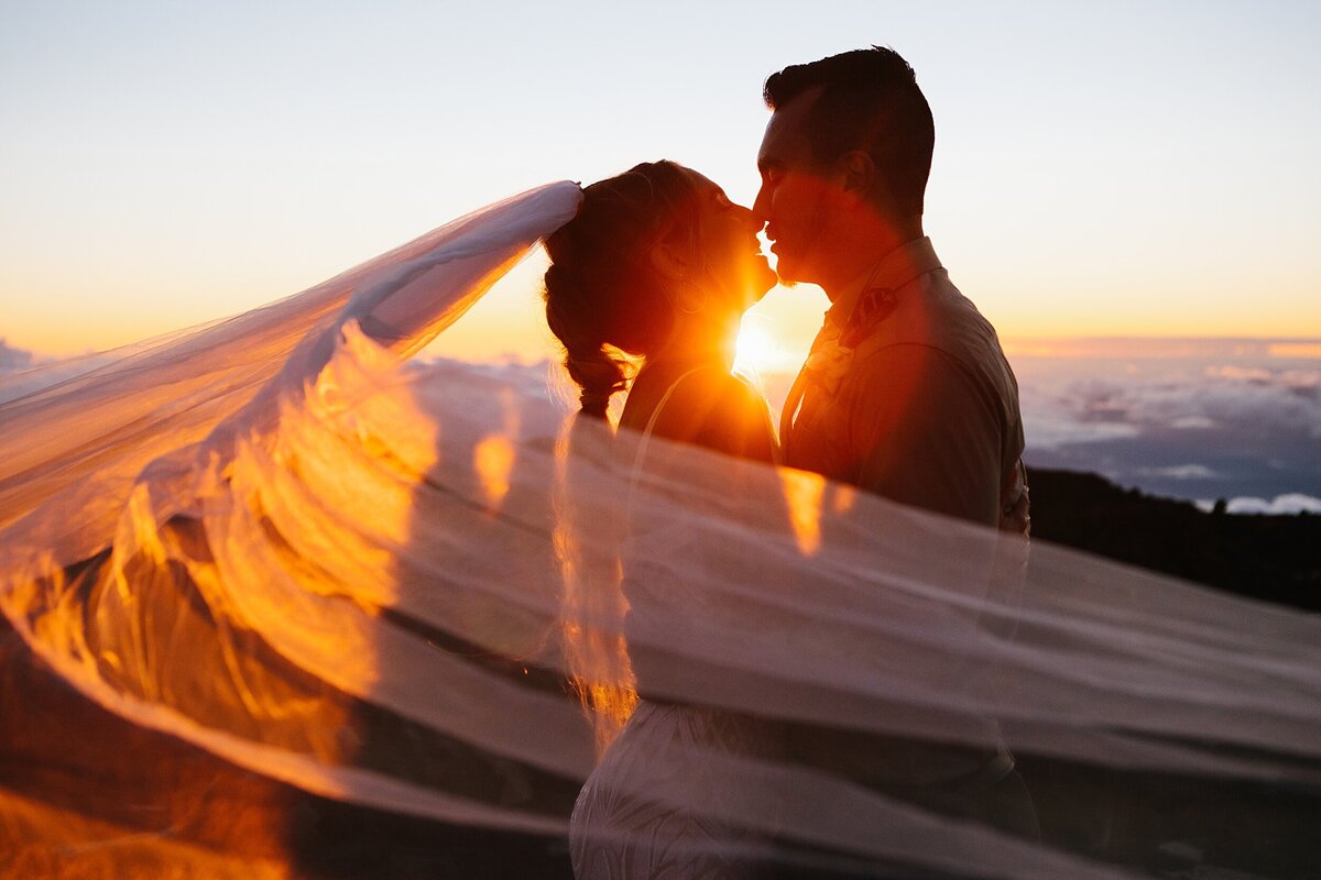 A bride and groom kiss during sunset at the summit of Haleakala national park in Hawaii