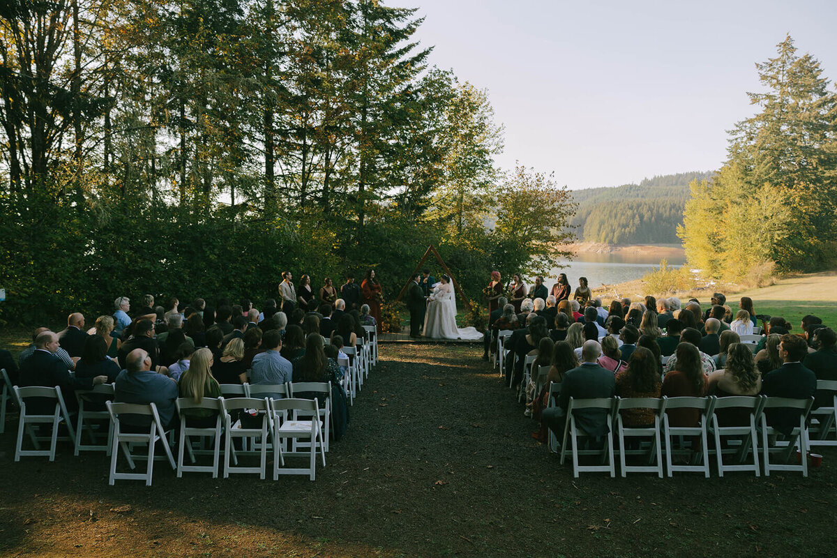 Wedding ceremony taking place by a lake at Sky Camp Oregon wedding venue.
