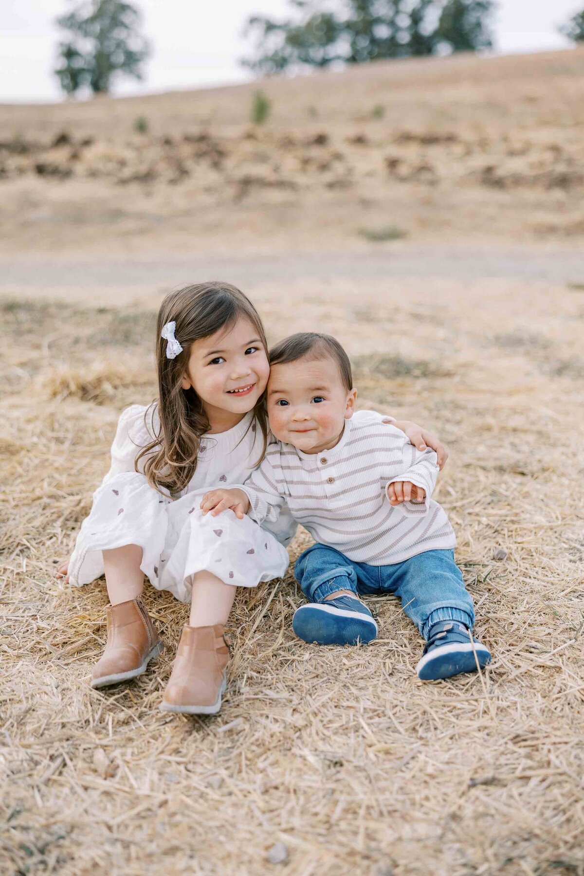 toddler sister and brother hugging each other and sitting on the ground