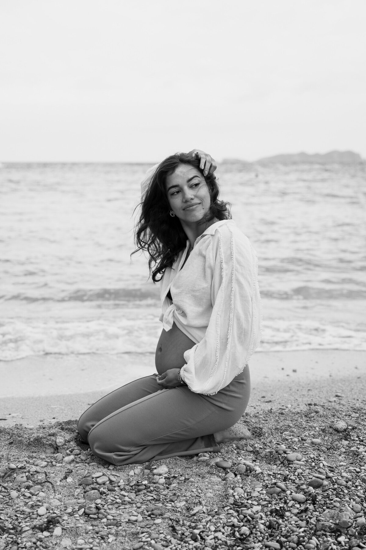 Pregnant woman is sitting on her knees on the beach on Ibiza for a pregnancy photoshoot