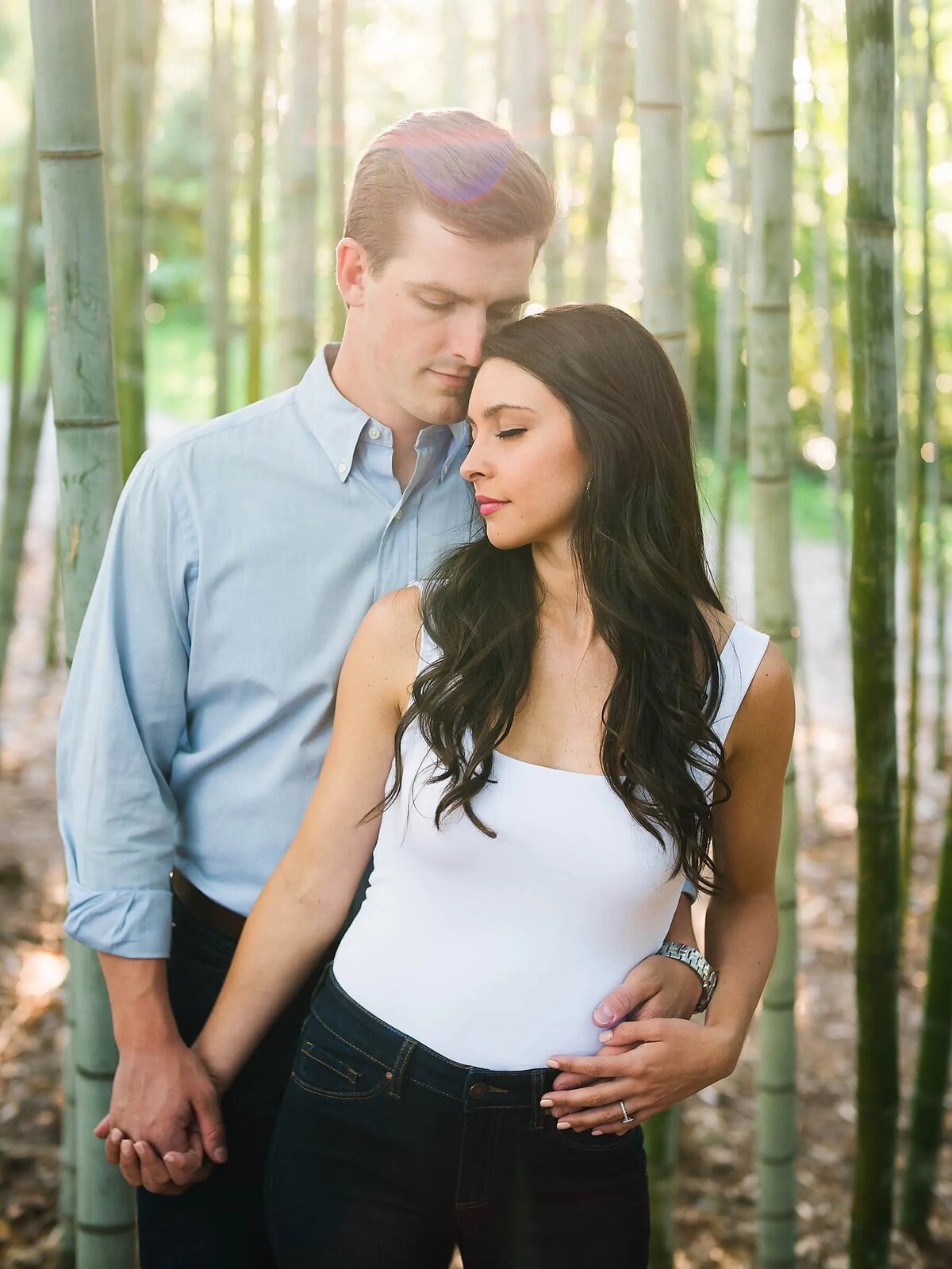 A man in a blue shirt and a woman in a white top holding hands in a serene bamboo grove.