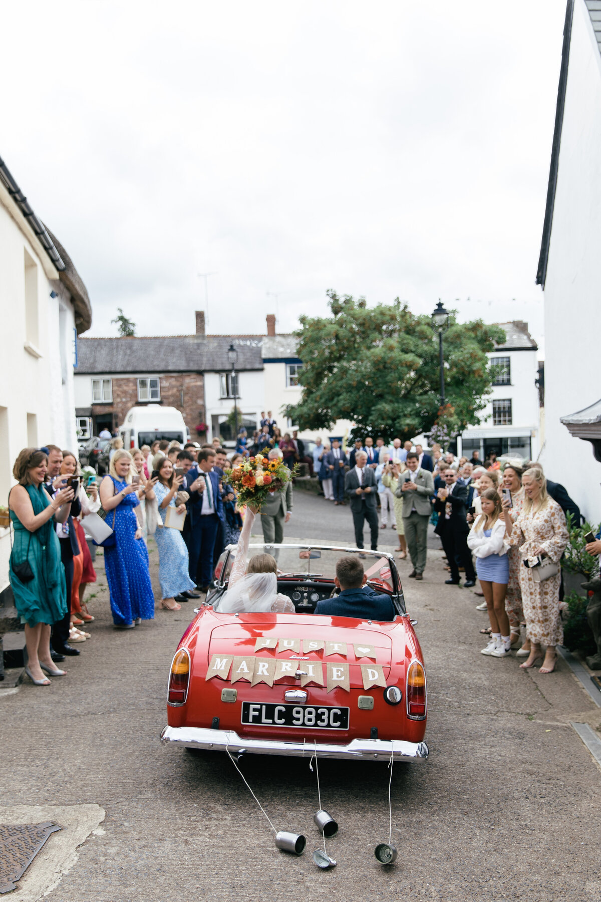 guests wave goodbye as couple leave in MG car to go to wedding reception
