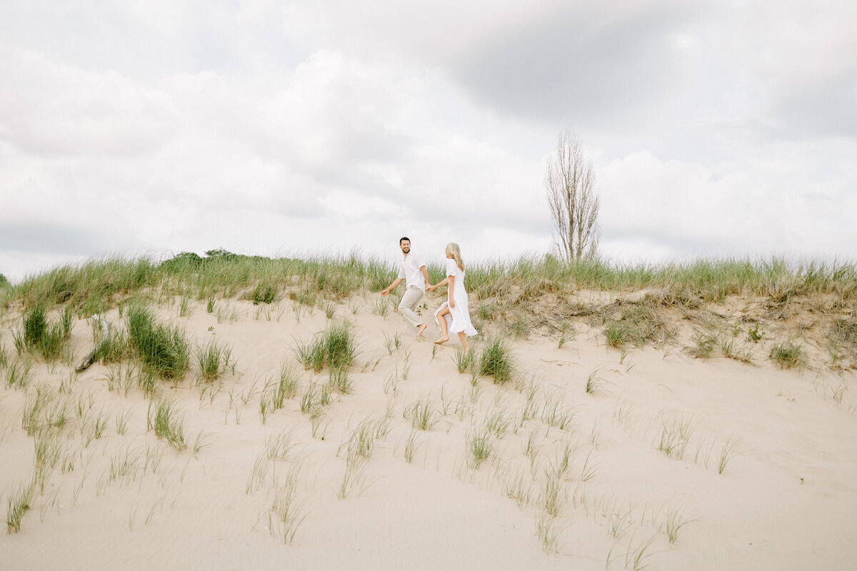 couple holding hands walking through sand dunes