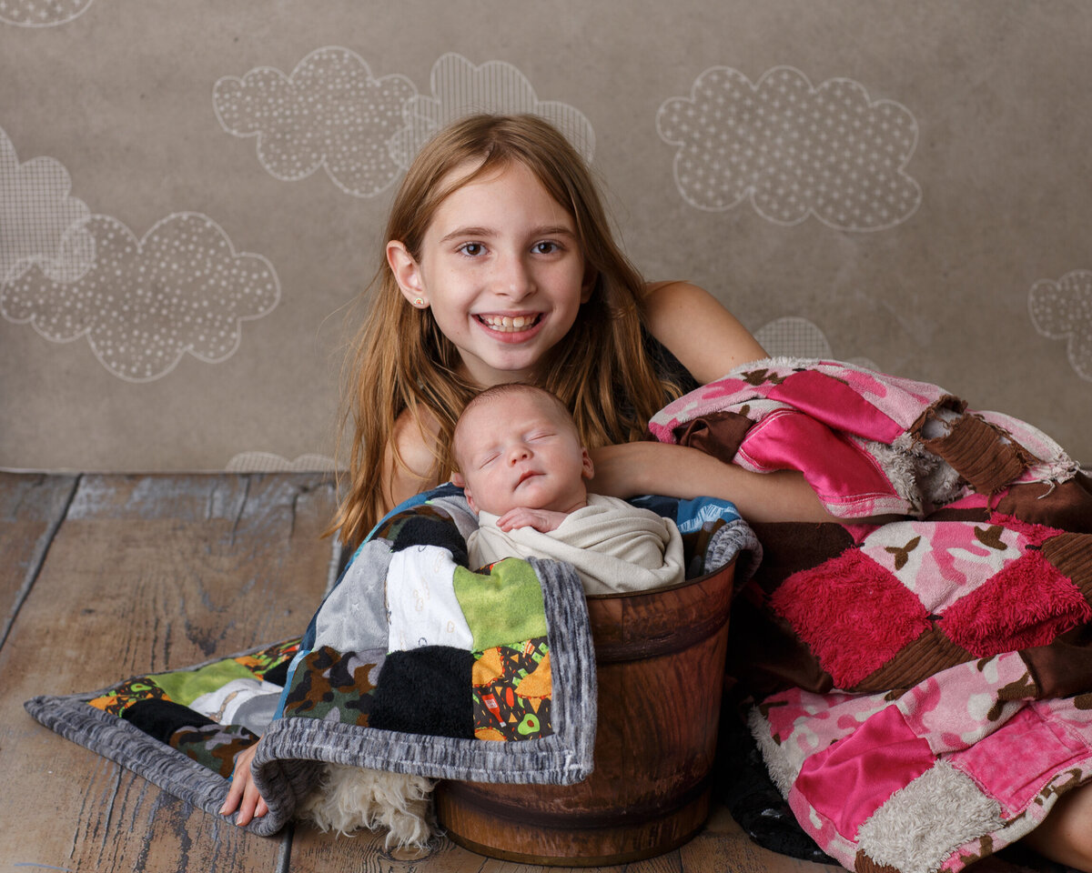Photo of a young girl laying down next to her baby brother who is sitting in a bucket