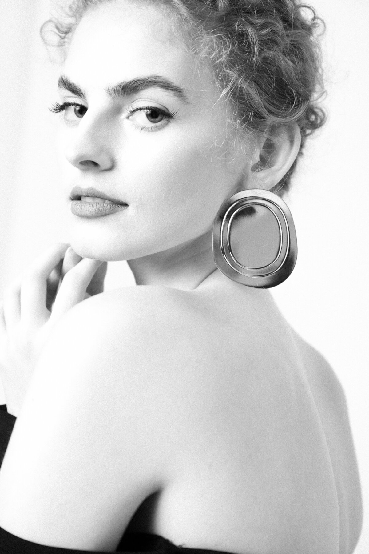 A headshot of a women showing her back and looking to the camera touching her chin with her hands