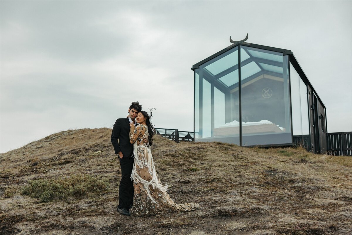 Bride and groom standing outside a modern glass cabin in Iceland during their elopement, photographed by a destination elopement photographer.