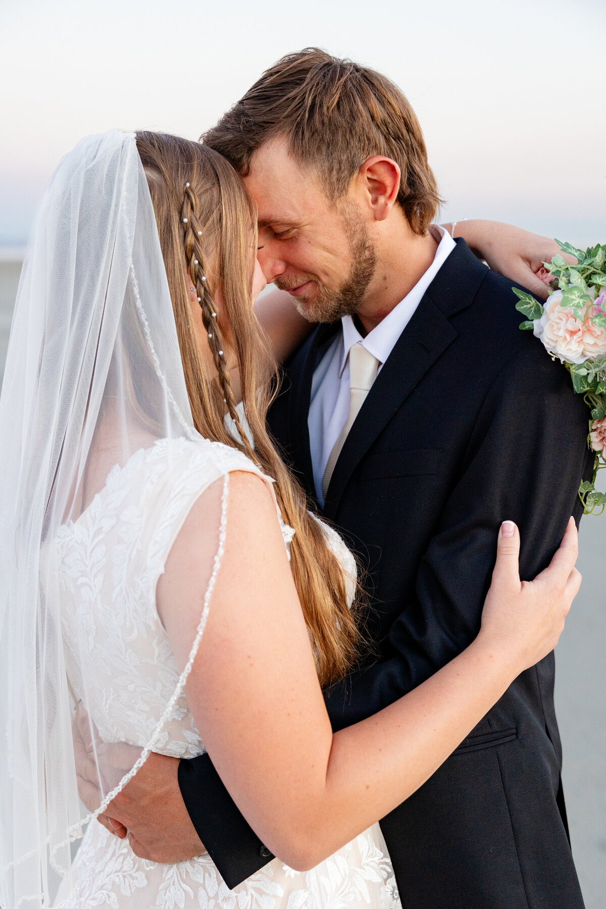  Bride and groom stand close, smiling as they embrace on the Salt Flats at sunrise.