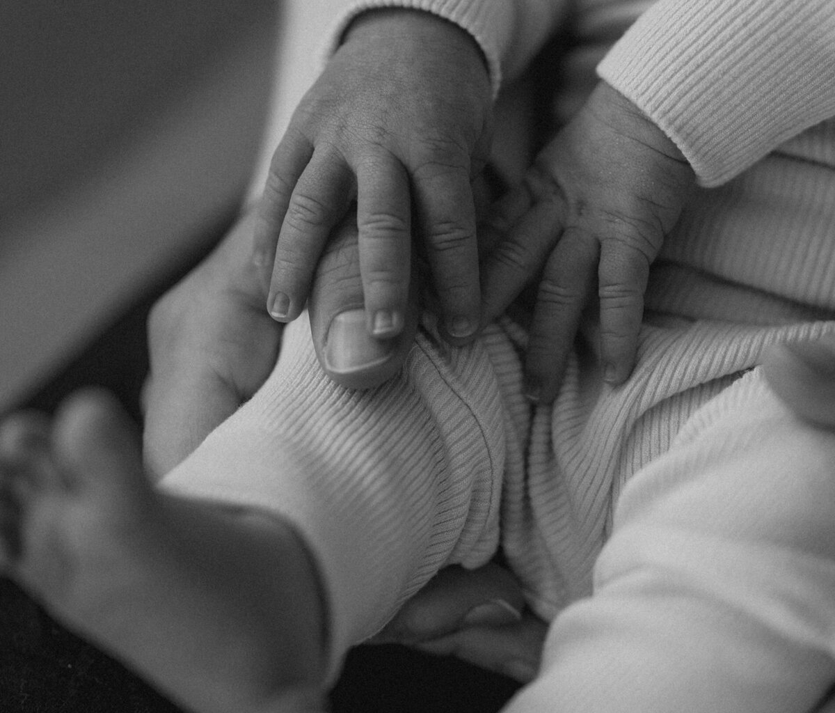 parents embracing newborn with closeup of tiny hands and toes