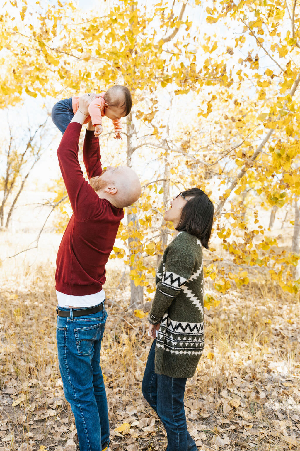 A parent holding their baby up in the air while their partner stands behind them.