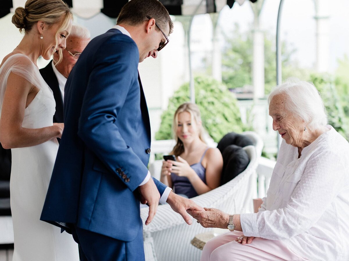 Brides's grandmother looking at the groom's wedding band with bride and other relatives looking at them.