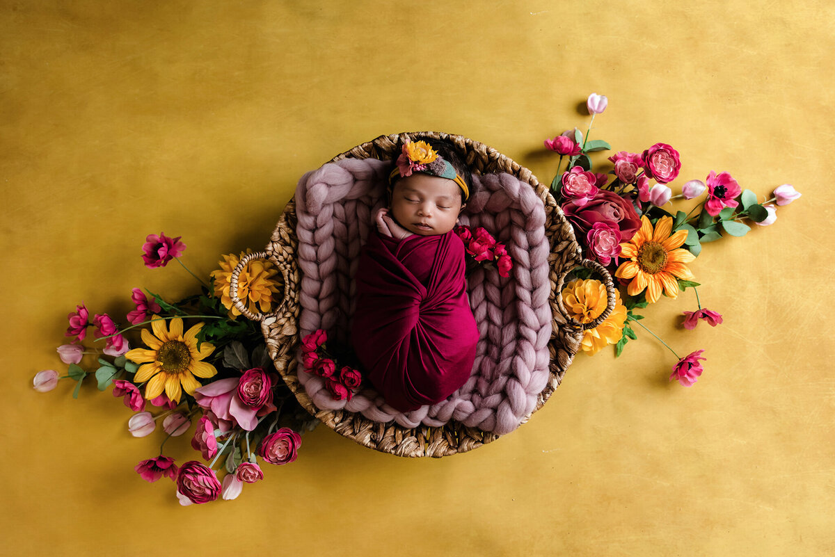 baby girl wrapped in pink sleeping in basket surrounded by pink and yellow flowers