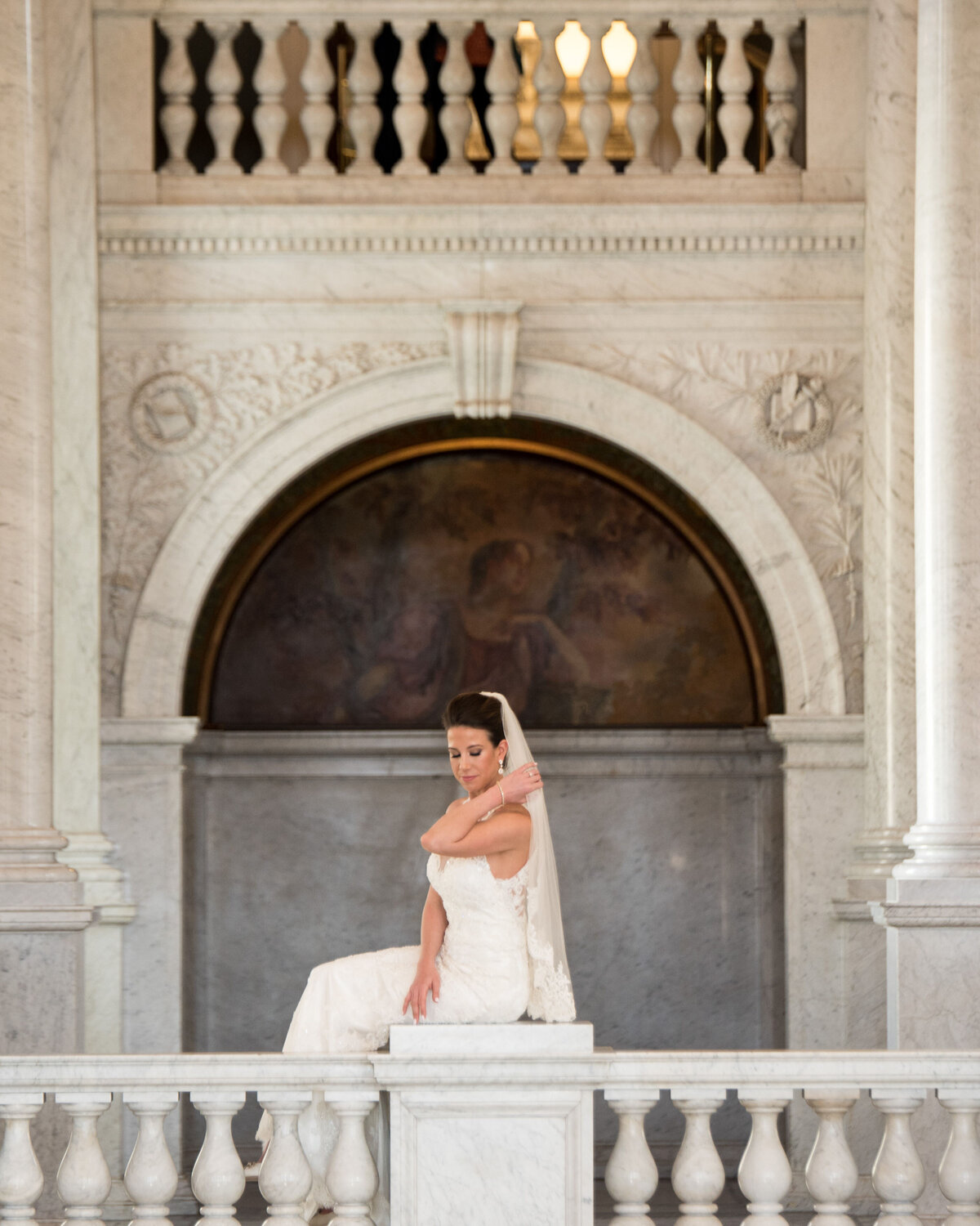 A person in a wedding dress sitting on a pillar looking over a balcony 