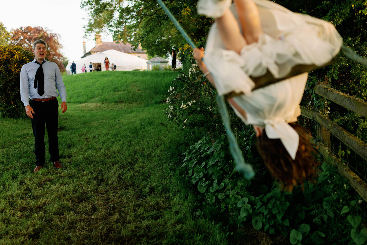 A wedding guest pushing a flower girl on a swing and her nearly falling off
