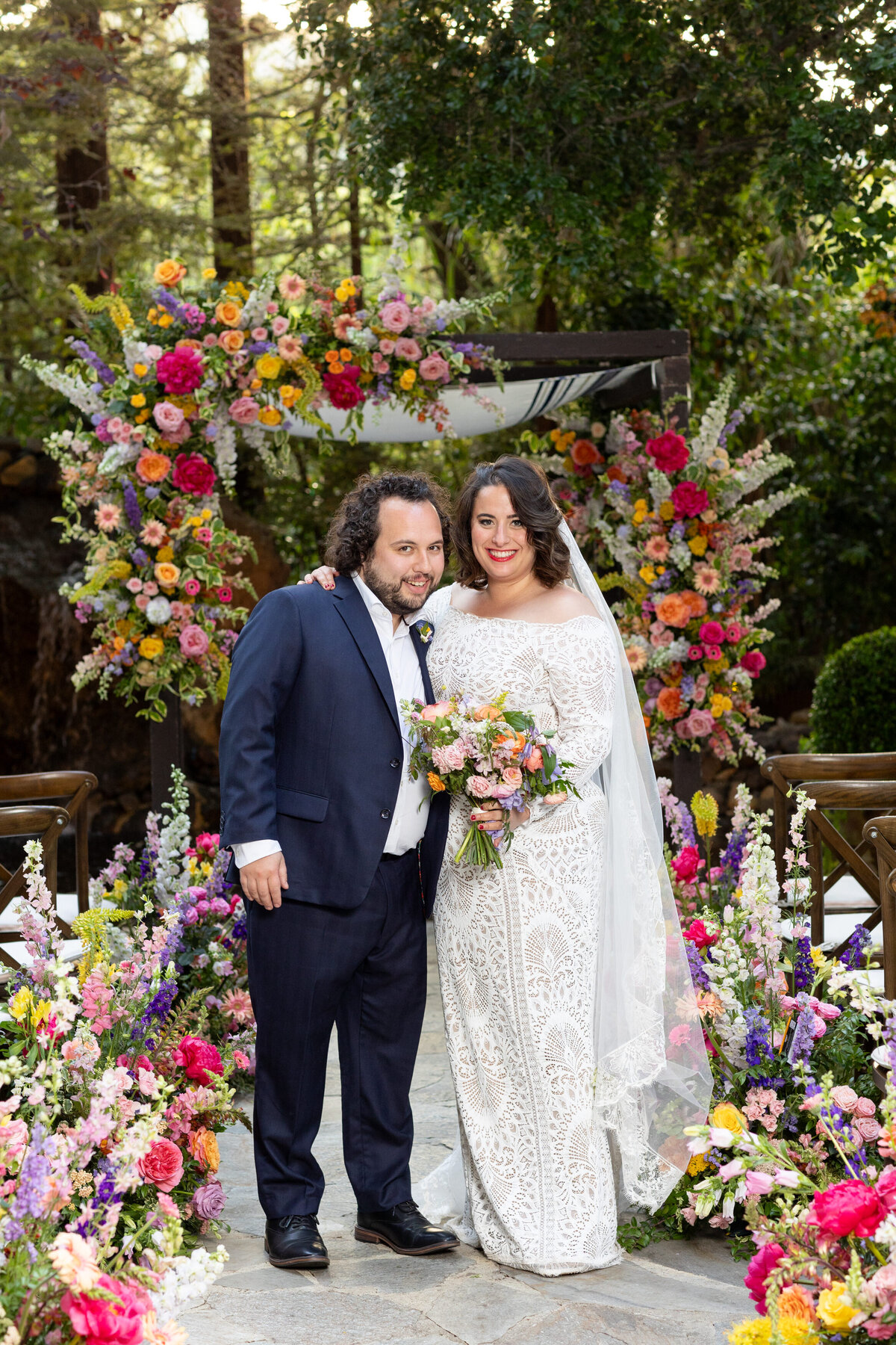 A wedding couple standing in the middle of an aisle surrounded by flowers