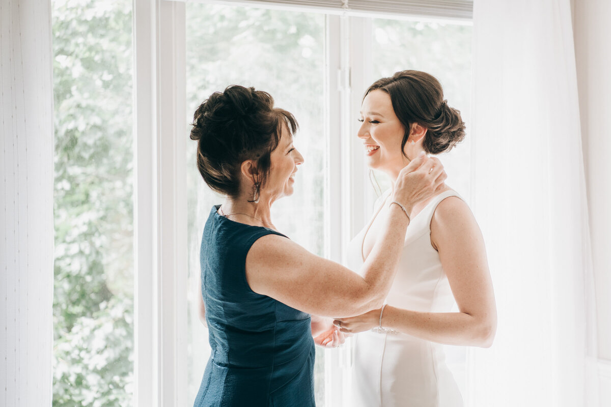 A mother of the bride helping the bride with her earrings