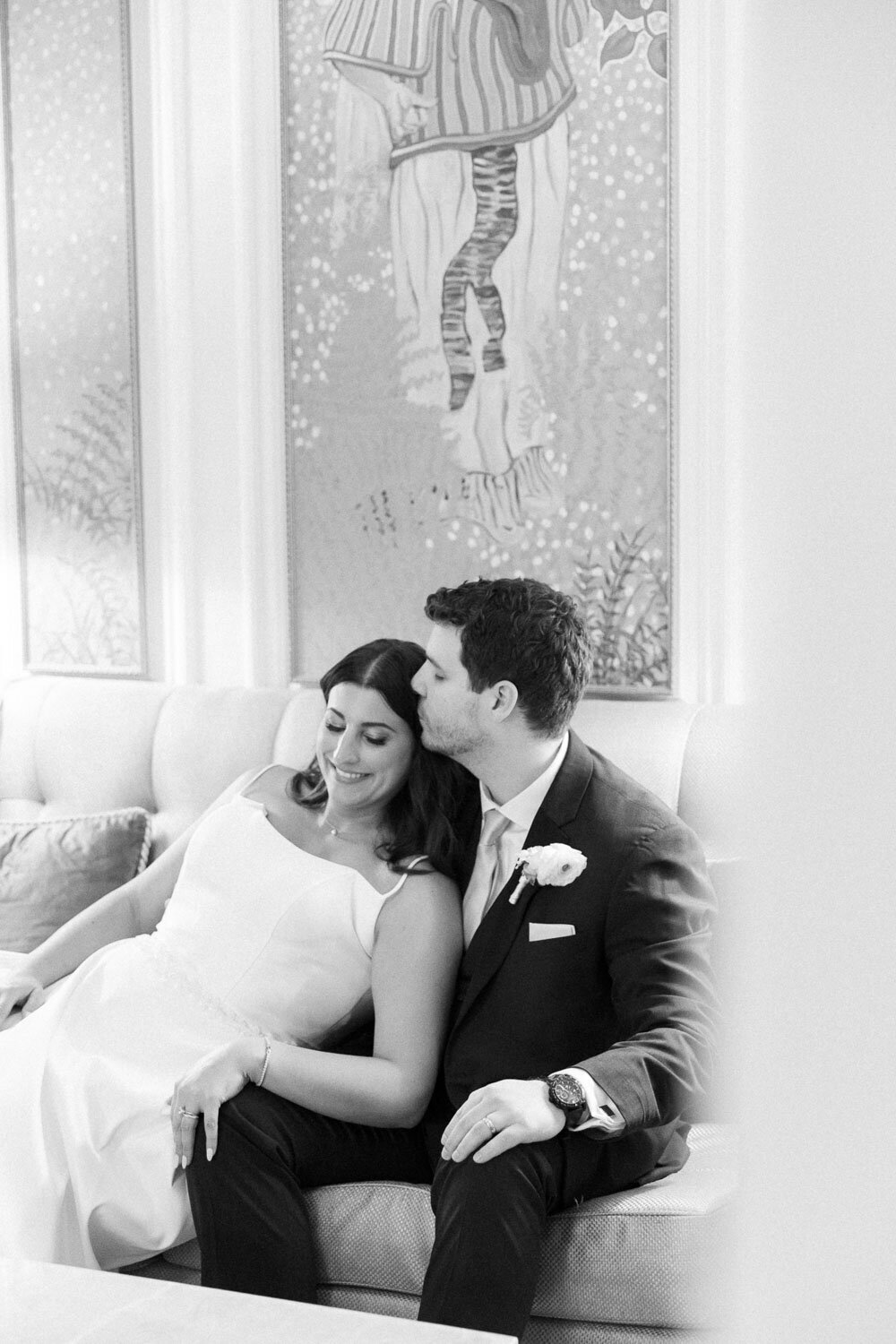 Groom kisses bride’s forehead while seated
