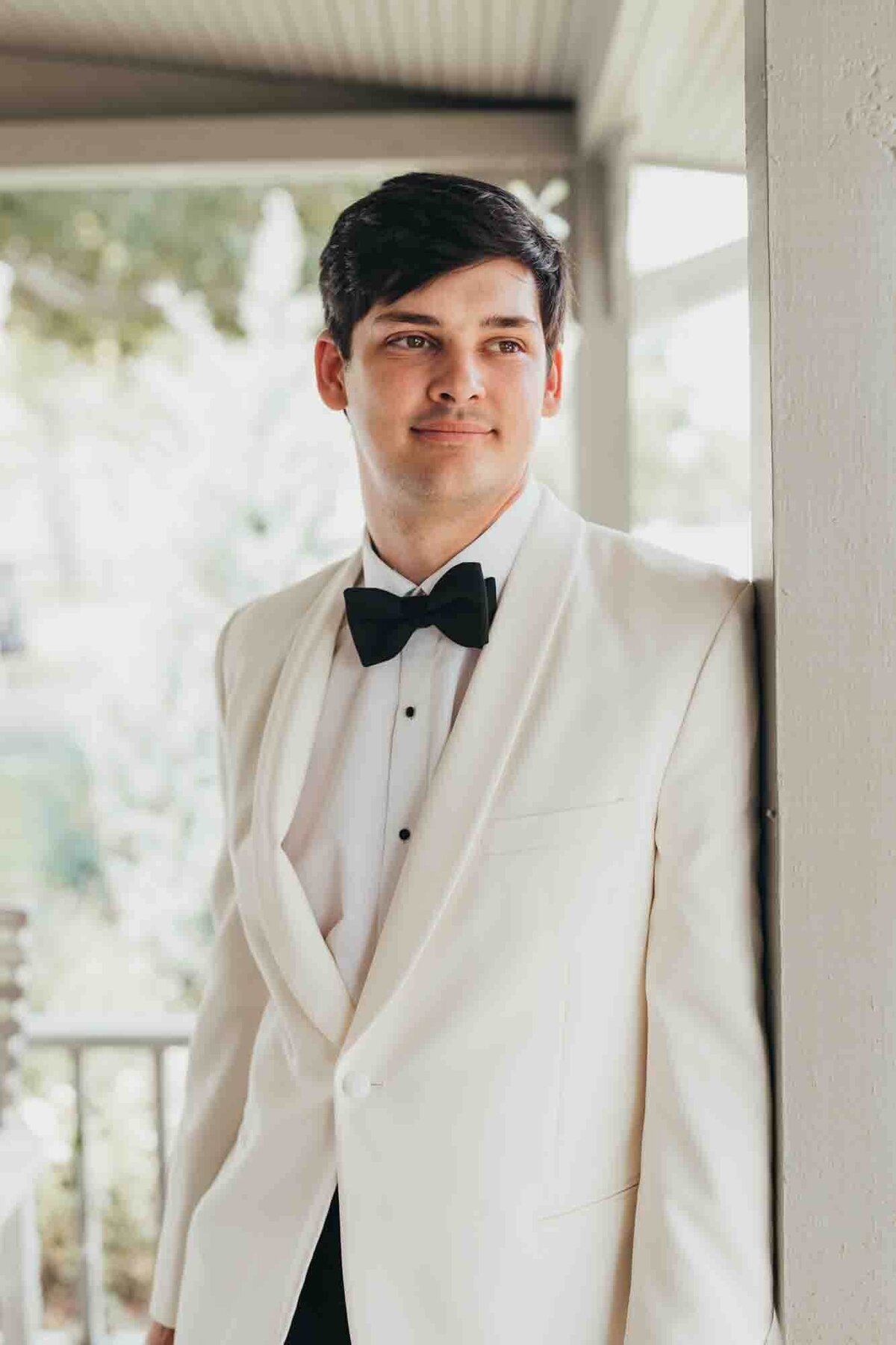 groom looks off into the distance minutes before his ceremony, wearing a white tux with black bow tie.