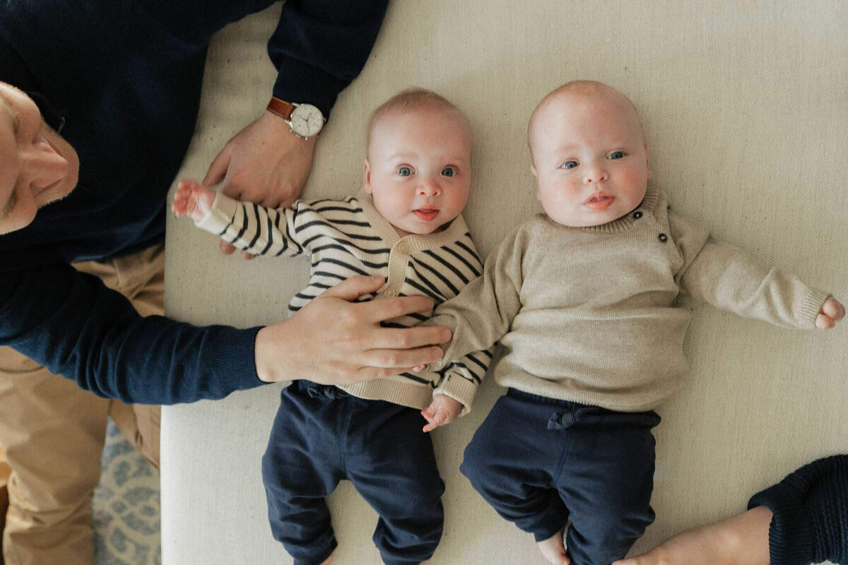 Twin babies laying on couch as mom and dad look on. Relaxed family photography at home in Cleveland.