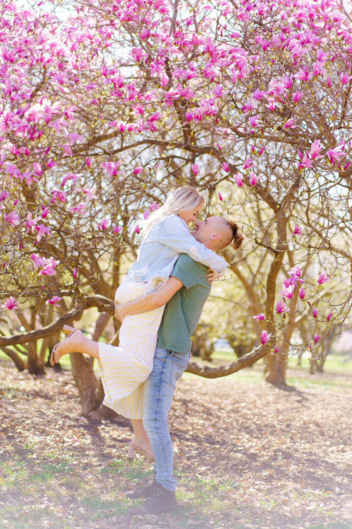 Man picks up his partner as she lifts one leg in front of pink magnolia trees - Goodale Park Columbus, Ohio.