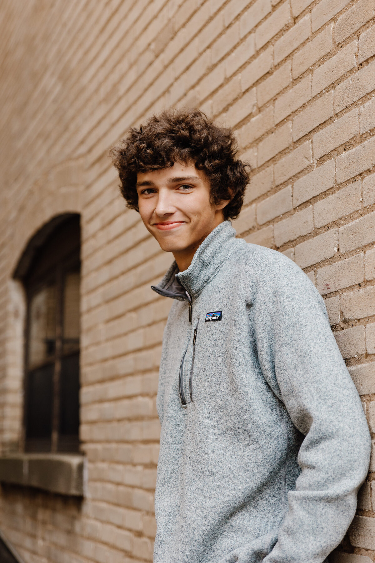 A boy smiling and leaning against a brick wall