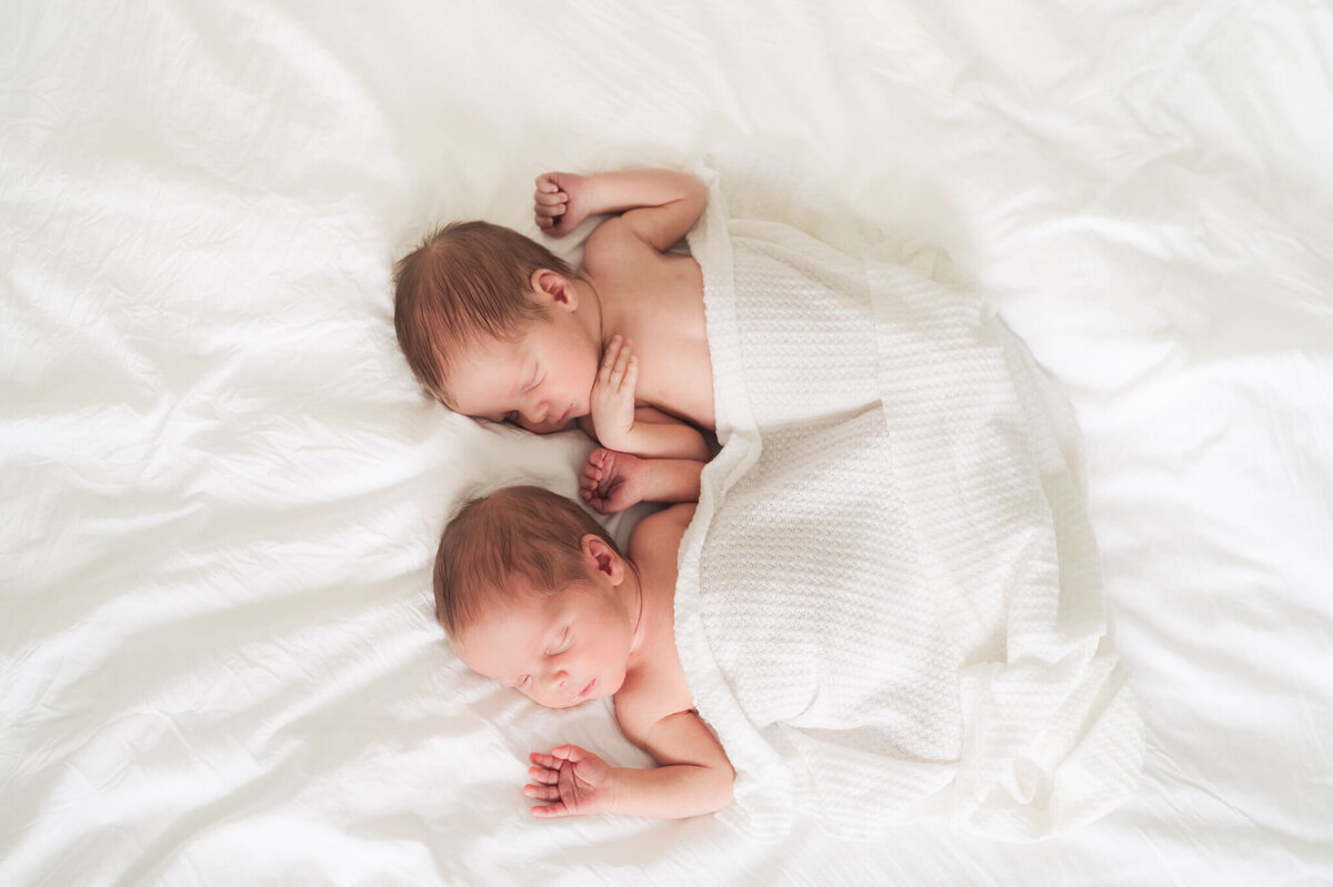 twin newborns laying on a bed getting professional photos taken