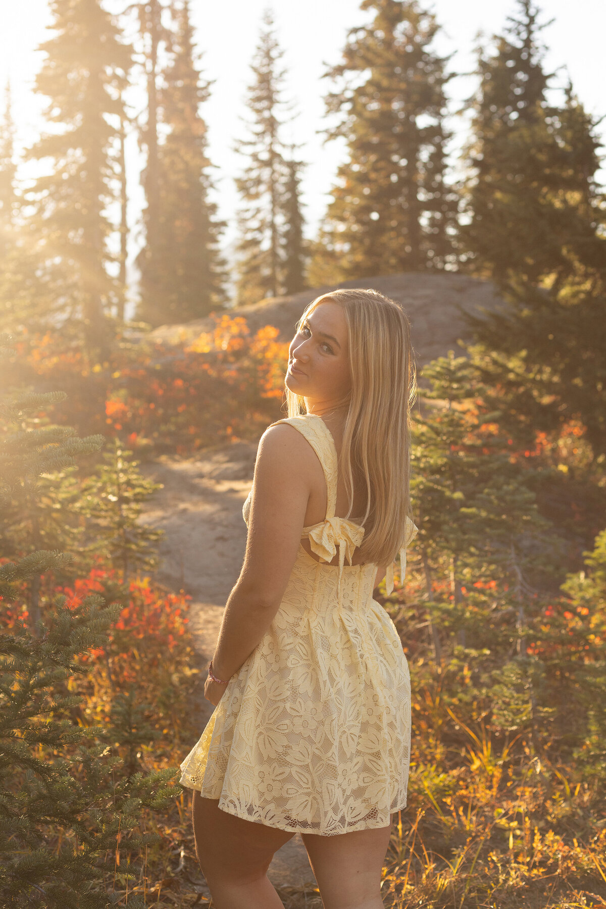 senior girl at mount rainier in autumn with yellow dress looking back at camera over left shoulder with sun haze