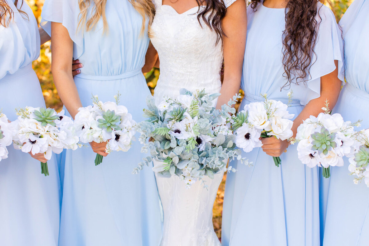 bridesmaids posing in blue dresses with white floral bouquets