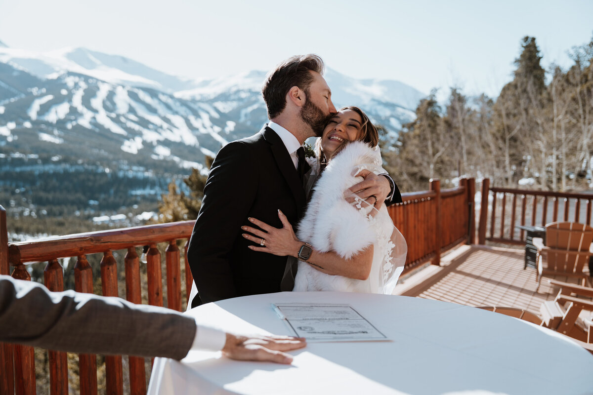 Newlyweds embrace after signing marriage license with snowy Breckenridge mountains behind them.